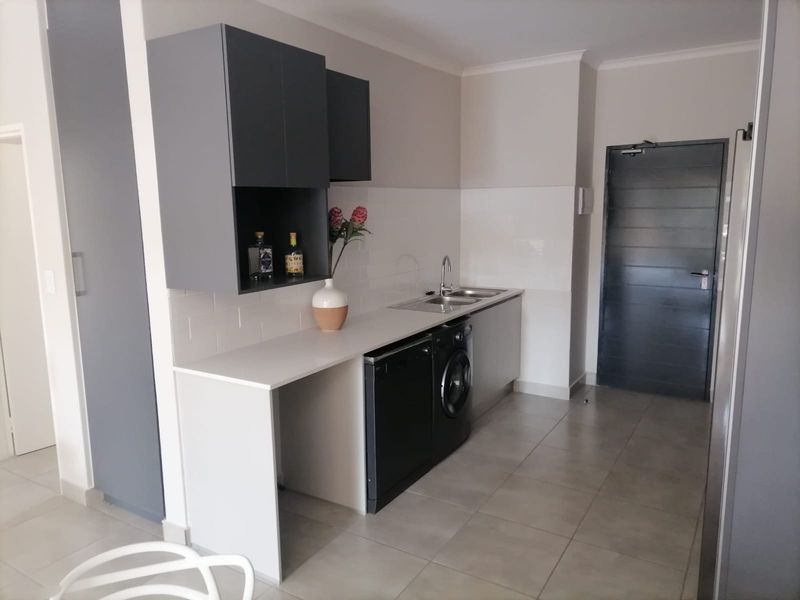 Modern kitchen area featuring sleek grey cabinetry, subway tile backsplash, tiled flooring, and integrated laundry and dishwasher appliances.