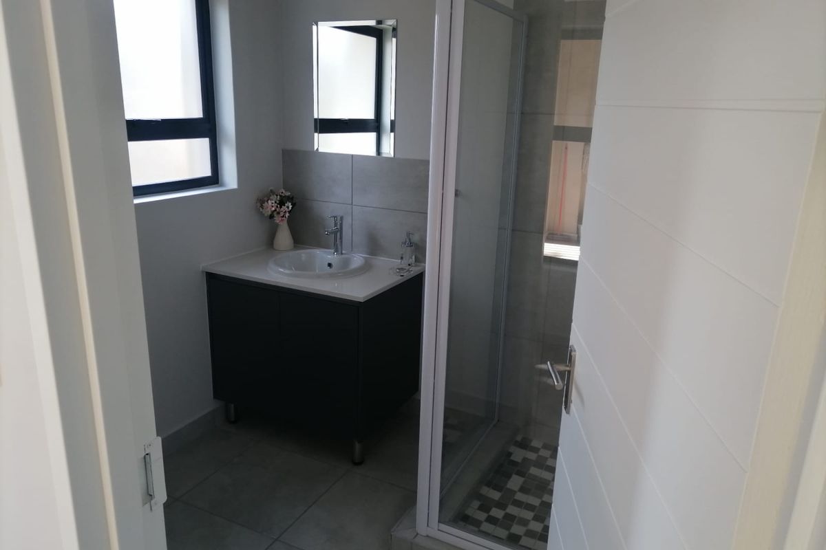 A modern bathroom featuring a vanity cabinet with a basin, a glass-enclosed shower, and neutral floor tiling.