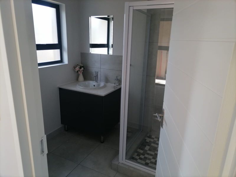 A modern bathroom featuring a vanity cabinet with a basin, a glass-enclosed shower, and neutral floor tiling.