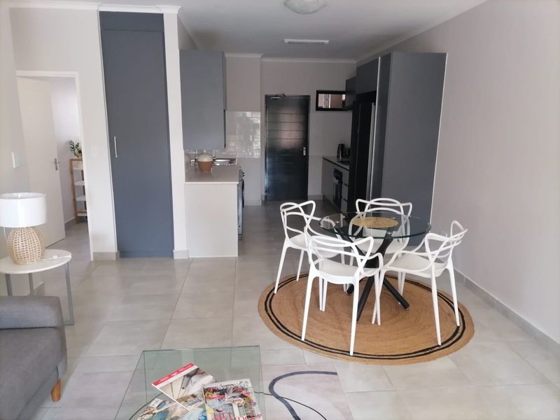 An open-plan living and dining area featuring modern grey built-in kitchen cabinetry, tiled flooring, and a functional layout.