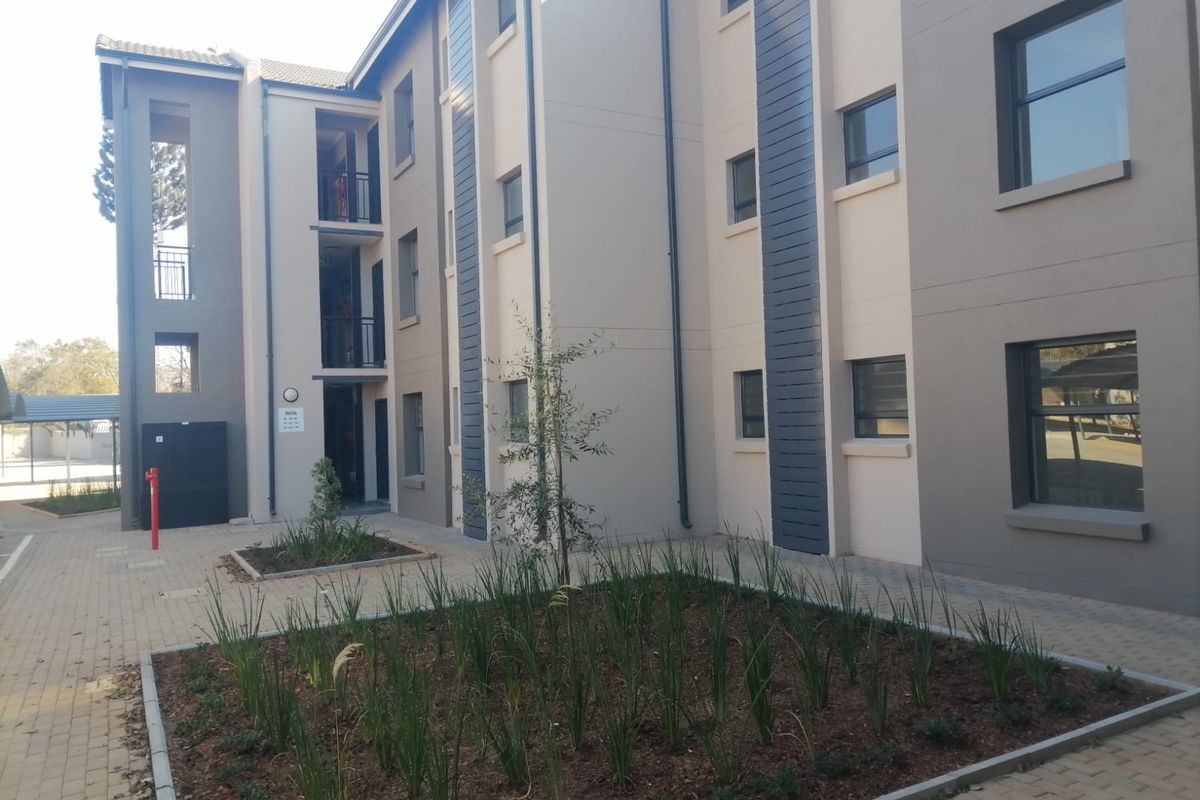 A view of a modern multi-story apartment building exterior featuring paved walkways, landscaped garden beds, and private balconies.