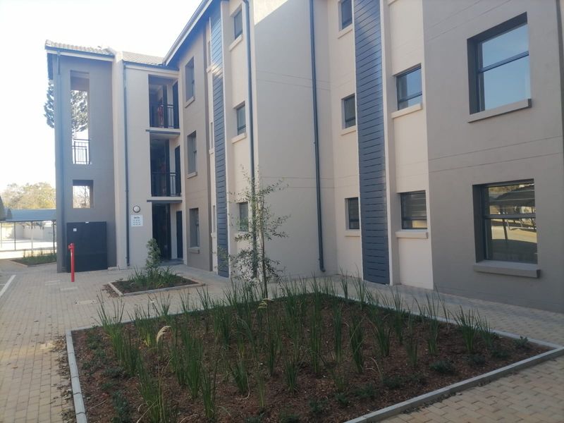 A view of a modern multi-story apartment building exterior featuring paved walkways, landscaped garden beds, and private balconies.