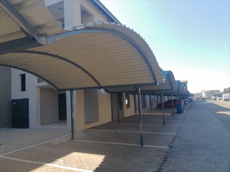 Covered parking area featuring a series of arched metal carports over paved parking bays adjacent to the apartment building.