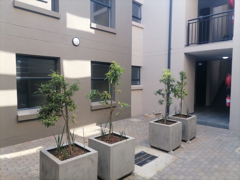 A clean, paved apartment courtyard featuring modern concrete planters, external wall lighting, and access to a stairwell with a fire hose reel.