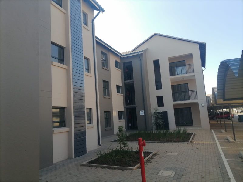 Exterior view of a modern apartment complex featuring paved walkways, landscaped garden beds, and covered parking bays.