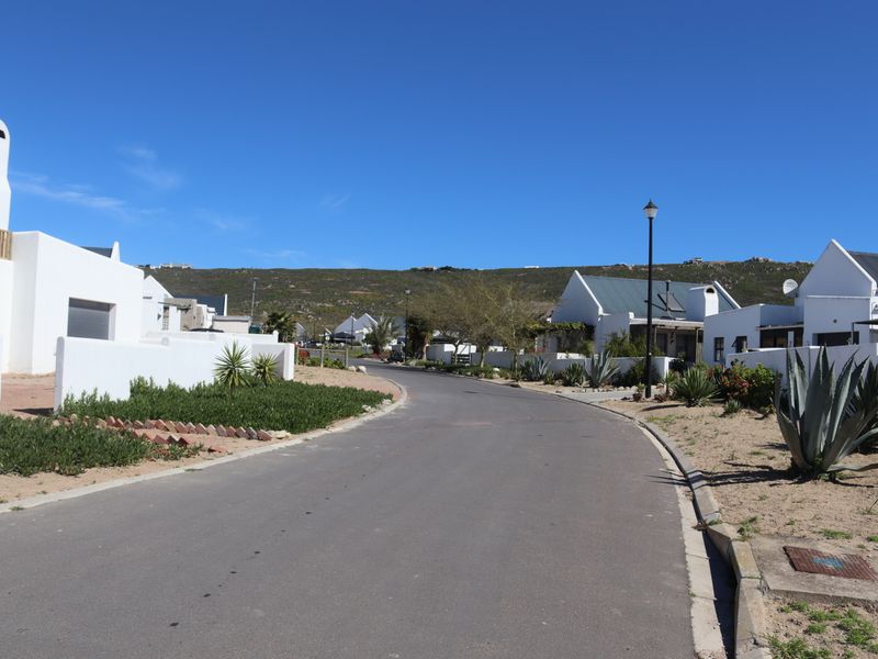 A clear street view of a residential estate featuring paved roads, well-maintained boundary walls, and established landscaping under a clear blue sky.
