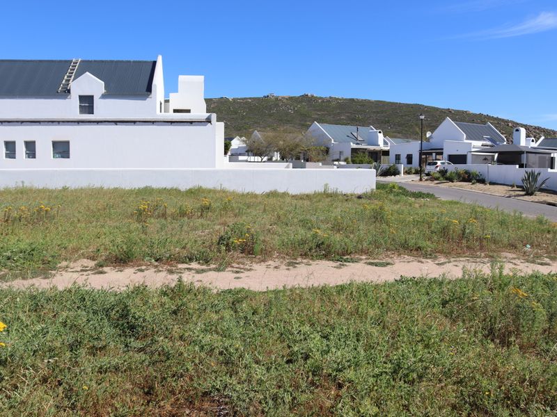 A vacant residential plot of land situated in a developed estate, featuring natural vegetation and adjacent to a paved street.