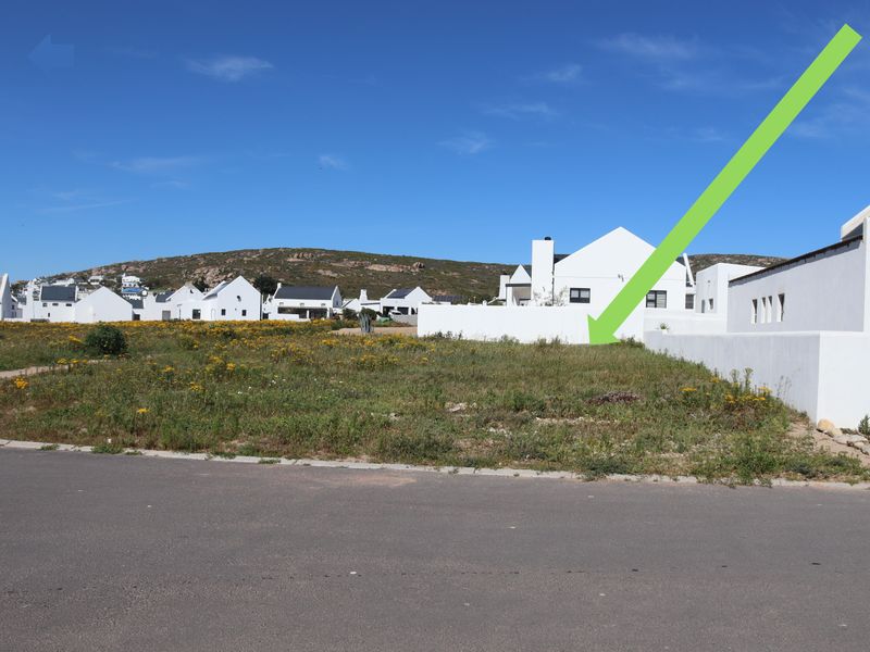 A vacant residential plot situated in a developed estate, featuring street frontage and adjacent boundary walls.