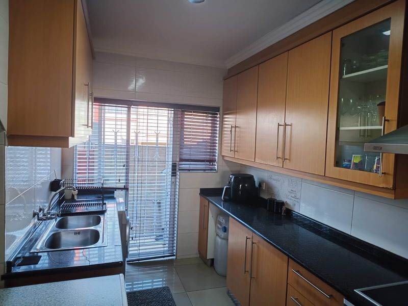 A functional kitchen featuring wooden cabinetry, granite countertops, a double bowl sink, and a tiled backsplash with direct access to an outdoor area.
