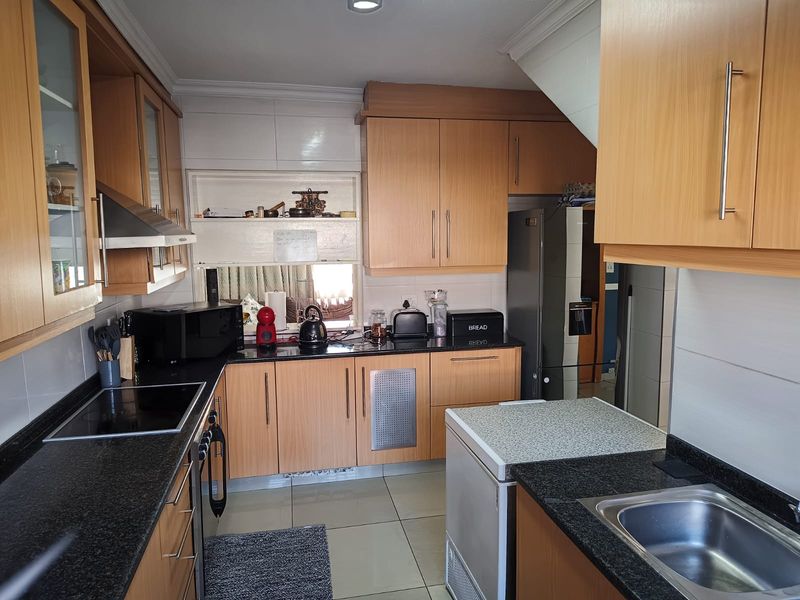 Functional kitchen featuring light wood cabinetry, dark granite countertops, integrated hob, extractor fan, and tiled flooring with a practical layout.