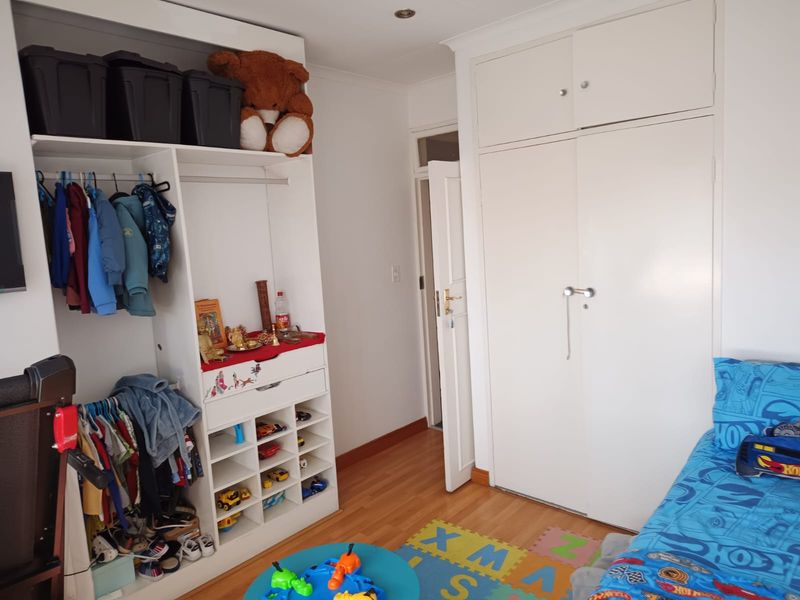 A bedroom featuring laminate flooring, a built-in wardrobe with overhead storage, and an integrated open shelving unit for storage.