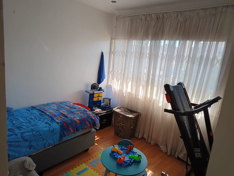A functional bedroom featuring laminate flooring, recessed lighting, and a large window fitted with a security gate and curtains.
