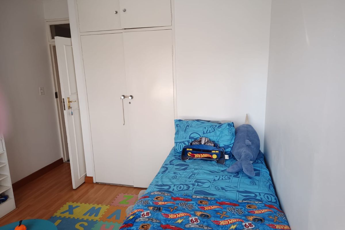 A functional bedroom featuring laminate flooring and a built-in wardrobe with overhead storage.