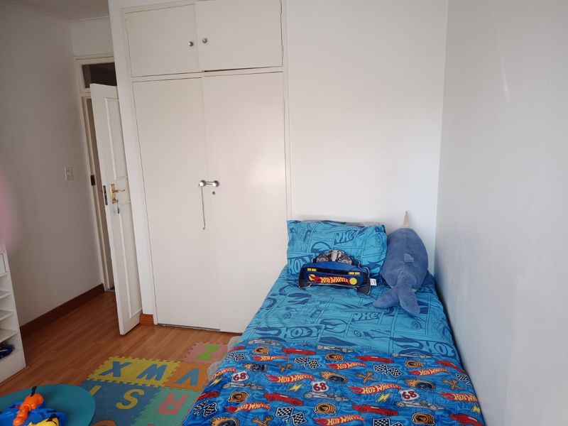 A functional bedroom featuring laminate flooring and a built-in wardrobe with overhead storage.
