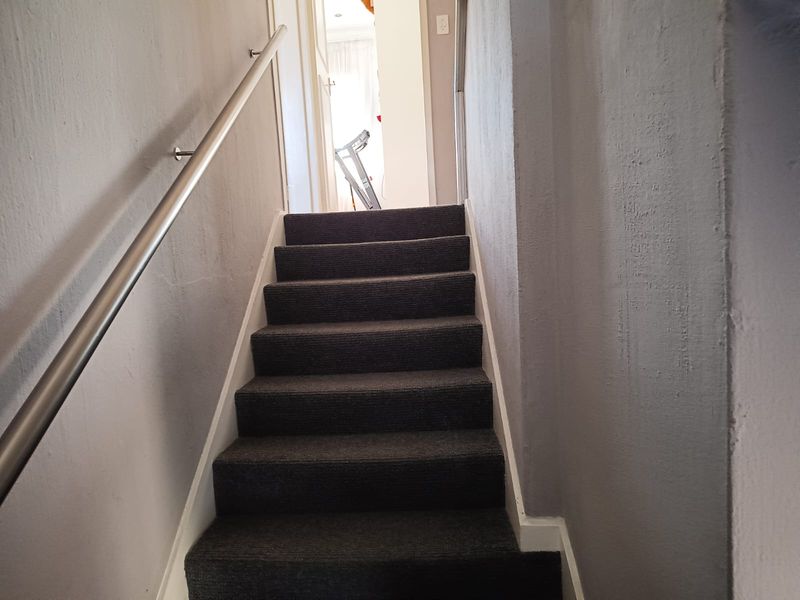 A functional staircase with dark carpeting and a modern metal handrail leading to an upper level landing.