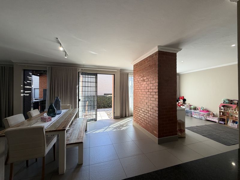 Spacious open-plan living and dining area featuring a distinctive exposed brick pillar, large sliding doors to the patio, and neutral tiled flooring throughout.