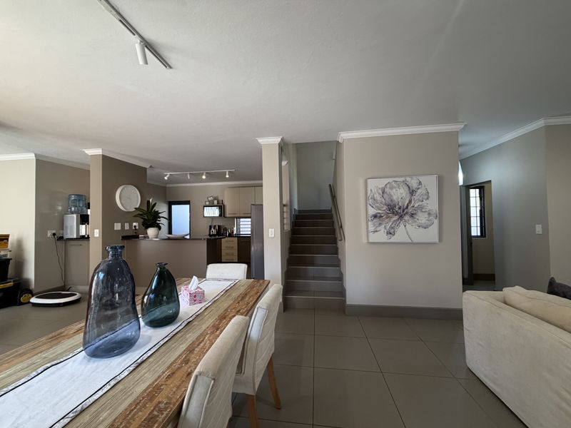 Spacious open-plan living and dining area featuring tiled floors, a central staircase, and a functional kitchen layout with neutral wall finishes.