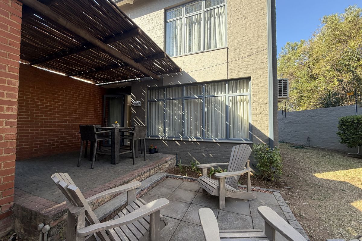 Rear exterior view of the townhouse featuring a covered patio with a timber pergola, paved terrace area, and brick wall finishes.