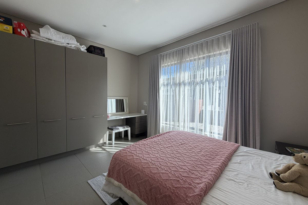 A well-maintained bedroom featuring neutral tiled flooring, ample built-in cupboard space, a integrated vanity, and large sliding doors providing natural light.