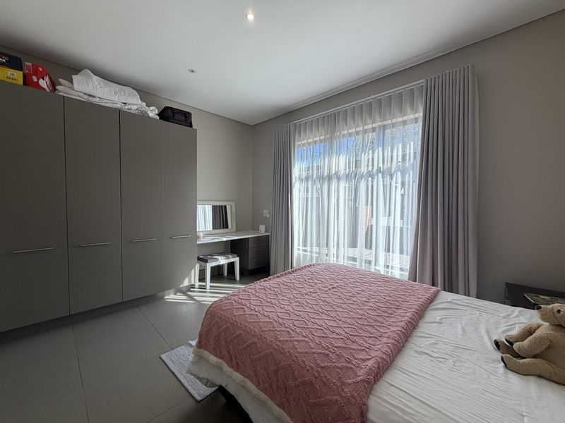 A well-maintained bedroom featuring neutral tiled flooring, ample built-in cupboard space, a integrated vanity, and large sliding doors providing natural light.
