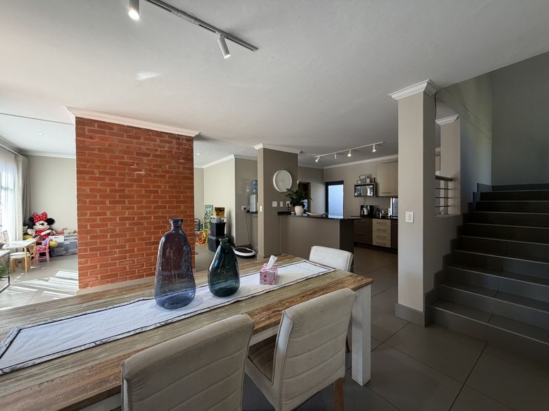 Spacious open-plan living and dining area featuring an exposed brick wall, tiled floors, and a staircase leading to the upper level.