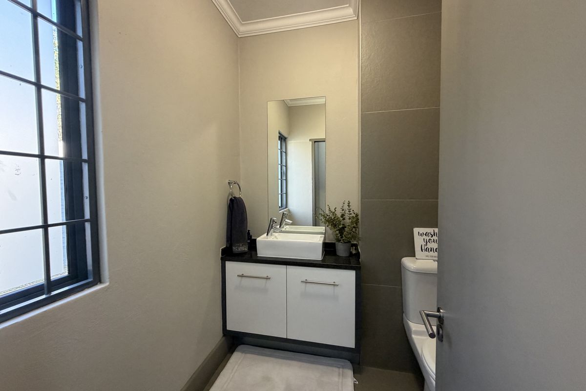 A modern guest bathroom featuring a sleek vanity with a vessel sink, a wall-mounted mirror, and neutral tiled accents.