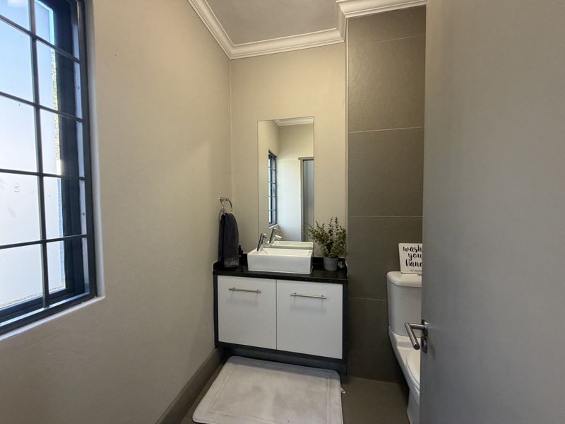 A modern guest bathroom featuring a sleek vanity with a vessel sink, a wall-mounted mirror, and neutral tiled accents.