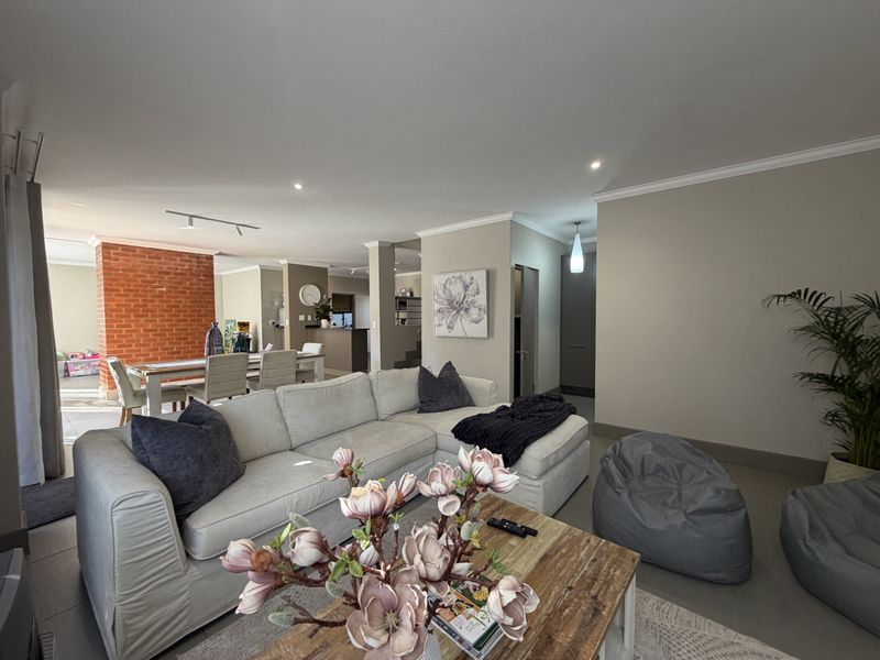 Spacious open-plan living and dining area featuring a striking exposed brick feature wall, neutral tiled flooring, and modern recessed lighting throughout.