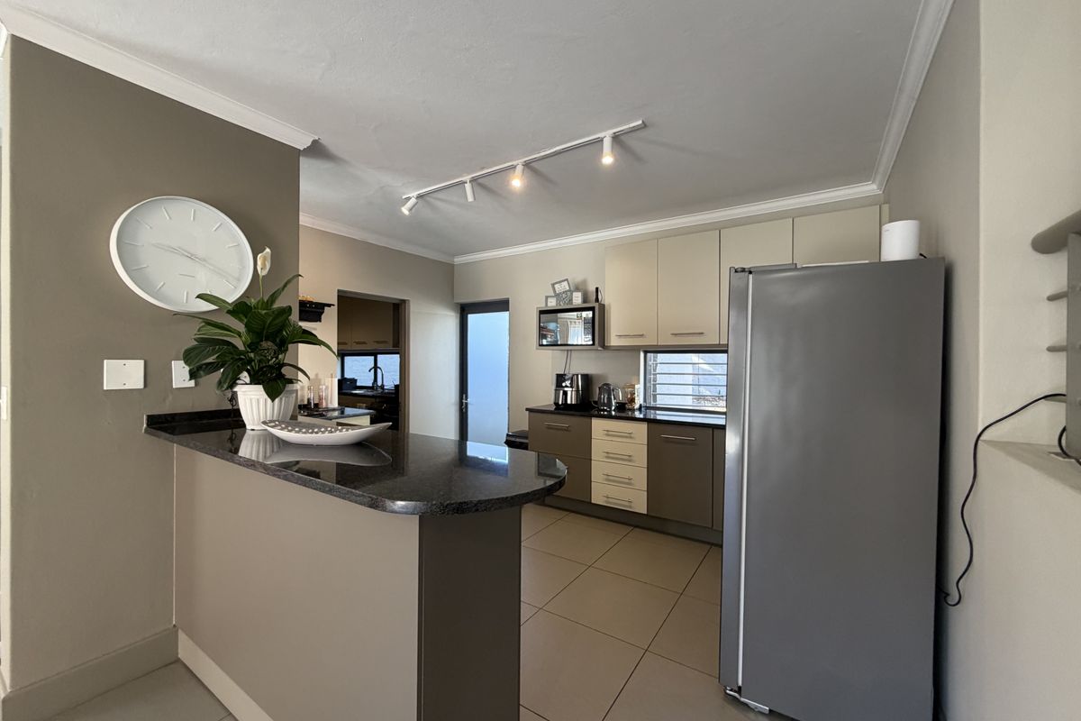 A functional kitchen featuring granite countertops, two-tone cabinetry, tiled flooring, and track lighting, with an adjacent breakfast bar and scullery access.