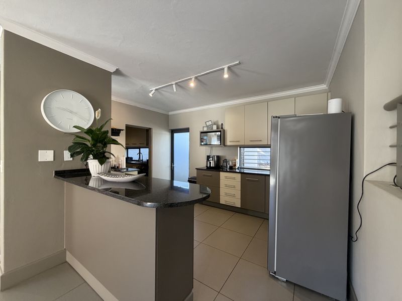 A functional kitchen featuring granite countertops, two-tone cabinetry, tiled flooring, and track lighting, with an adjacent breakfast bar and scullery access.
