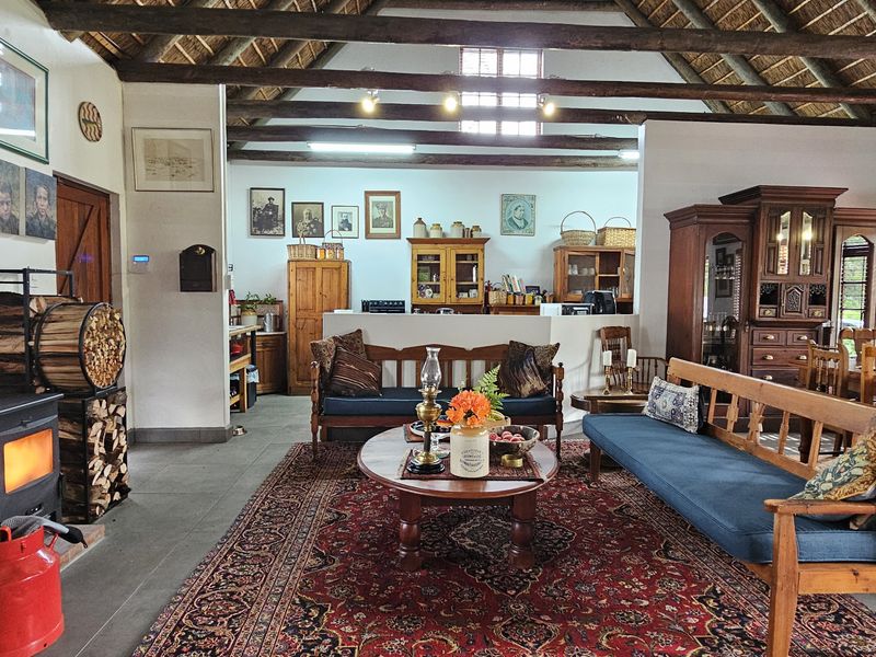 Spacious open-plan living and dining area featuring a high thatched ceiling with exposed timber beams and a cozy wood-burning fireplace.