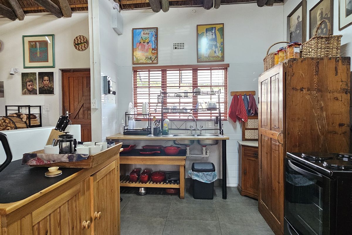Rustic kitchen featuring exposed timber ceiling beams, tiled flooring, timber cabinetry, and a freestanding electric stove with a double sink setup.