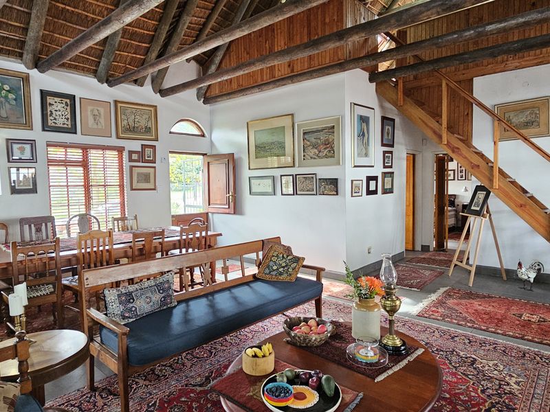 Spacious open-plan living and dining area featuring high vaulted ceilings with exposed timber rafters, a wooden staircase, and large windows providing natural light.