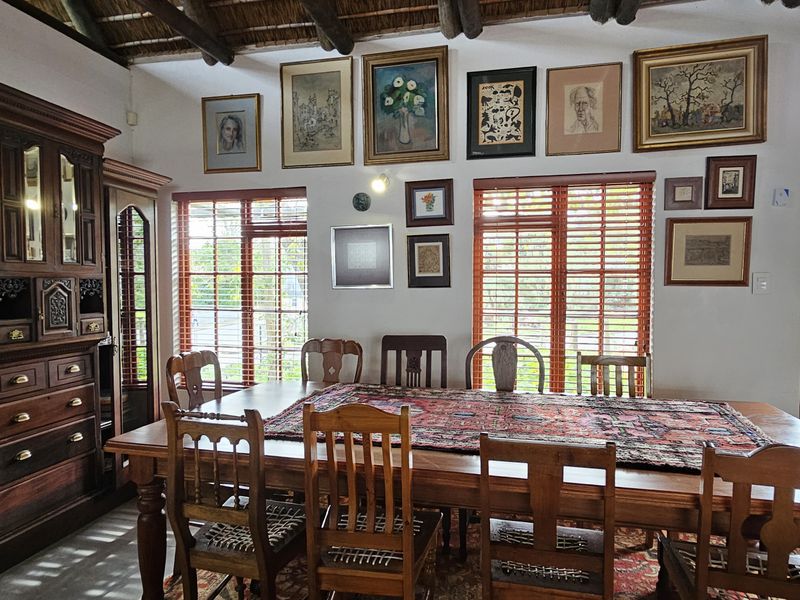 Dining room featuring exposed timber rafters, a thatched ceiling, and large windows with timber blinds, offering a warm and rustic atmosphere.