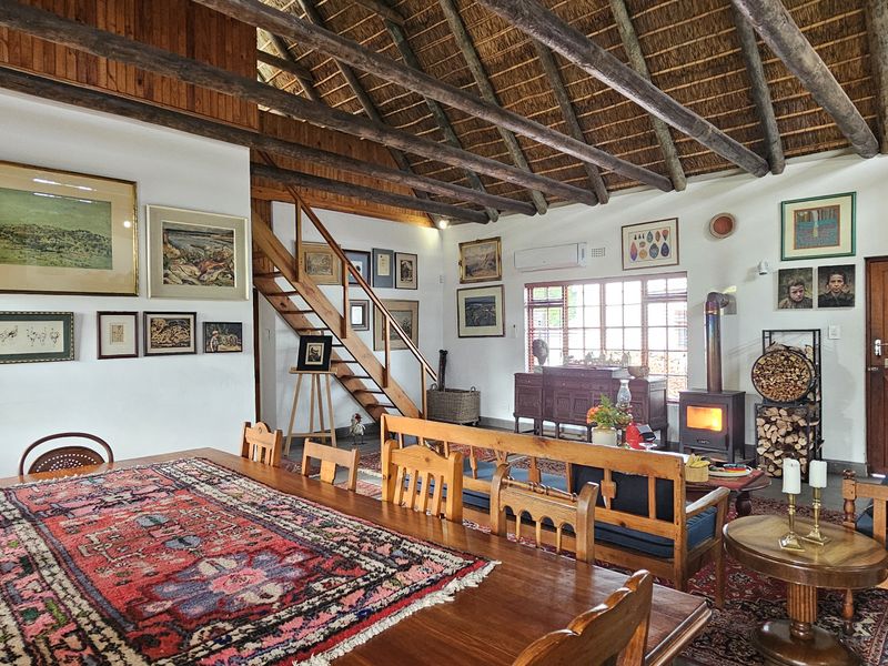 Spacious open-plan living and dining area featuring a high thatched ceiling with exposed timber rafters, a wood-burning stove, and a timber staircase.