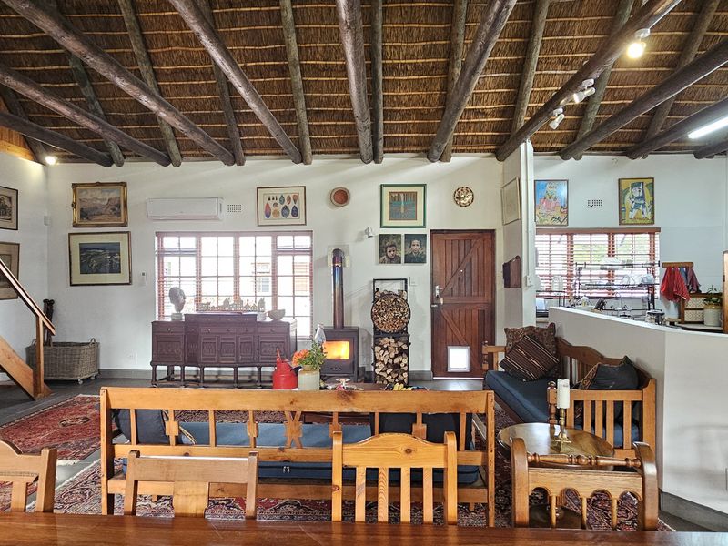 Spacious open-plan living area featuring a high vaulted thatched ceiling with exposed timber beams, a wood-burning stove, and an integrated kitchen space.