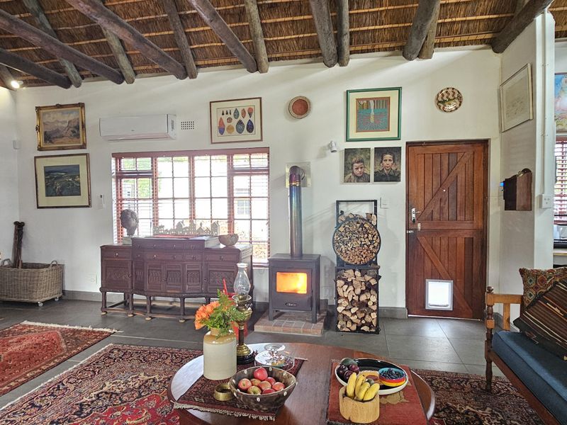 Spacious open-plan living area featuring a high exposed timber beam ceiling, thatched roof, wood-burning stove, and a timber staircase.