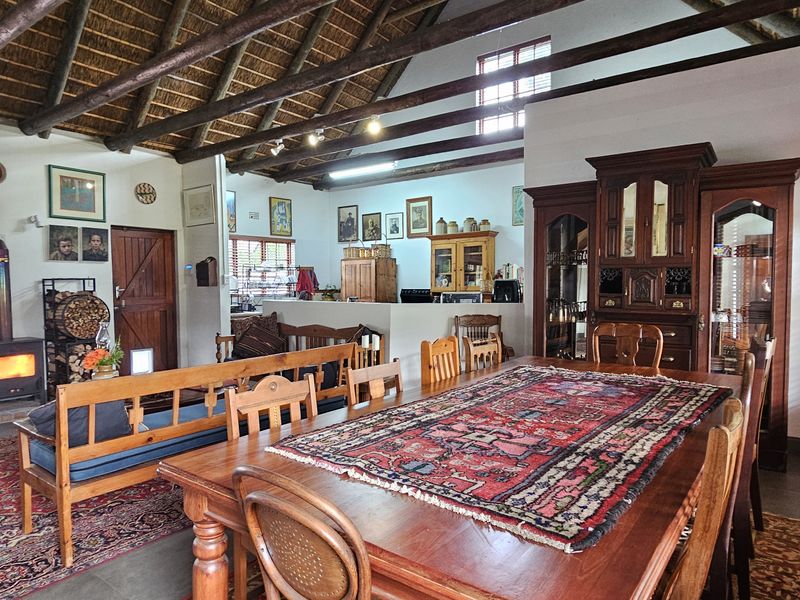 Spacious open-plan living and dining area featuring a high vaulted thatched ceiling with exposed timber rafters and a cozy wood-burning fireplace.