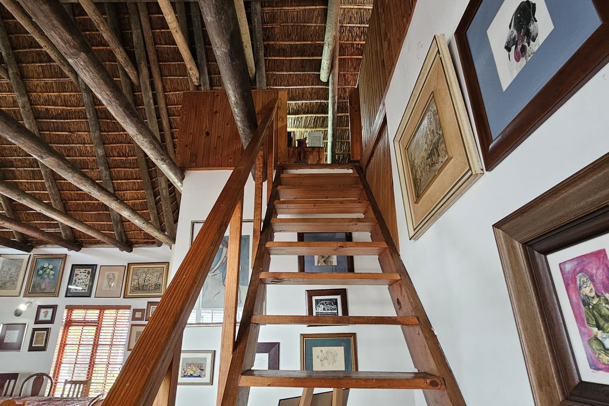 A living area featuring a high-pitched thatched roof with exposed timber rafters and a central wooden staircase leading to an upper level.