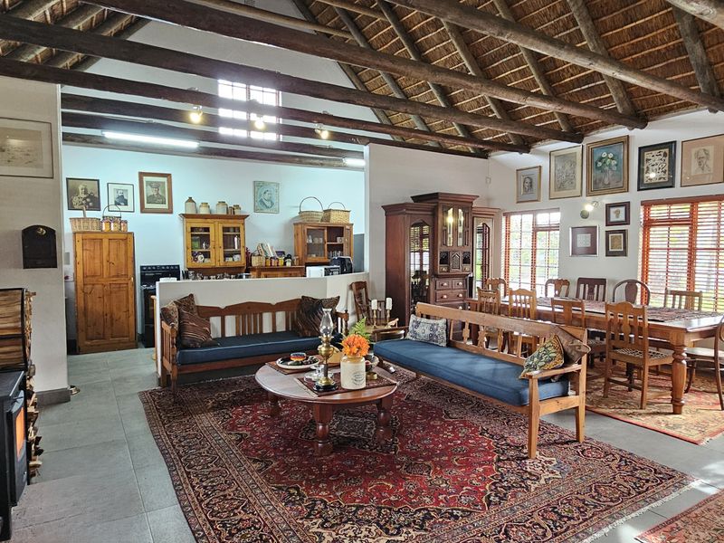 Spacious open-plan living and dining area featuring high vaulted ceilings with exposed timber rafters, a wood-burning fireplace, and tiled flooring throughout.
