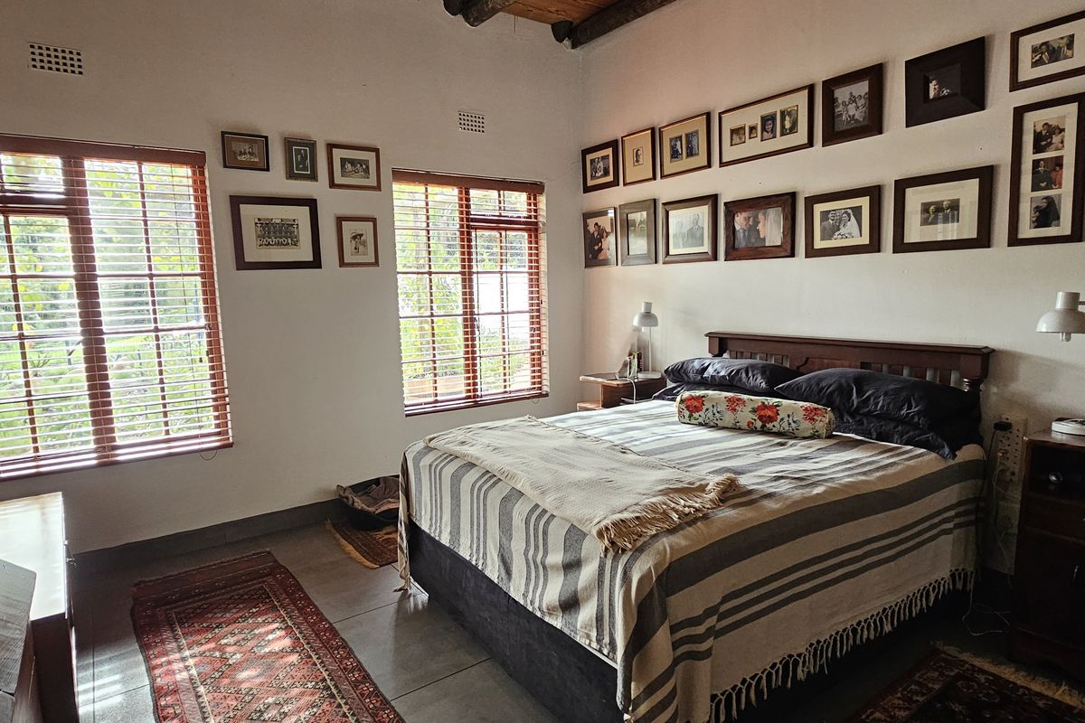A well-maintained bedroom featuring exposed timber ceiling beams, tiled flooring, and large timber-framed windows that provide ample natural light.