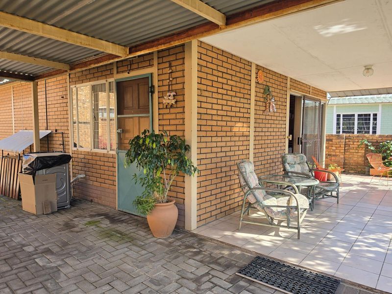 A covered outdoor patio area featuring brick walls, tiled flooring, and a corrugated metal roof, providing a functional space for outdoor relaxation.
