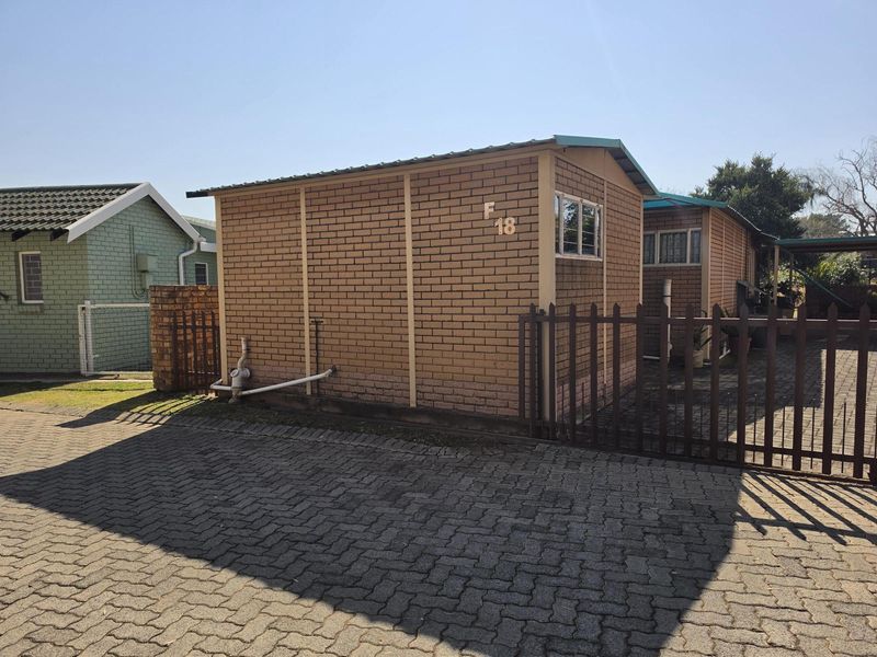Exterior view of a brick-built residential unit featuring a paved driveway and secure metal fencing.
