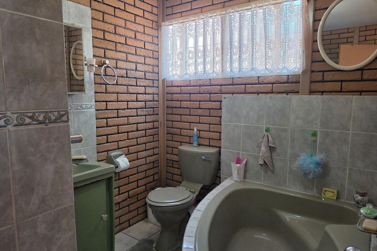 A dated bathroom featuring exposed brick walls, a built-in bathtub, a toilet, and a vanity cabinet with tiled finishes.