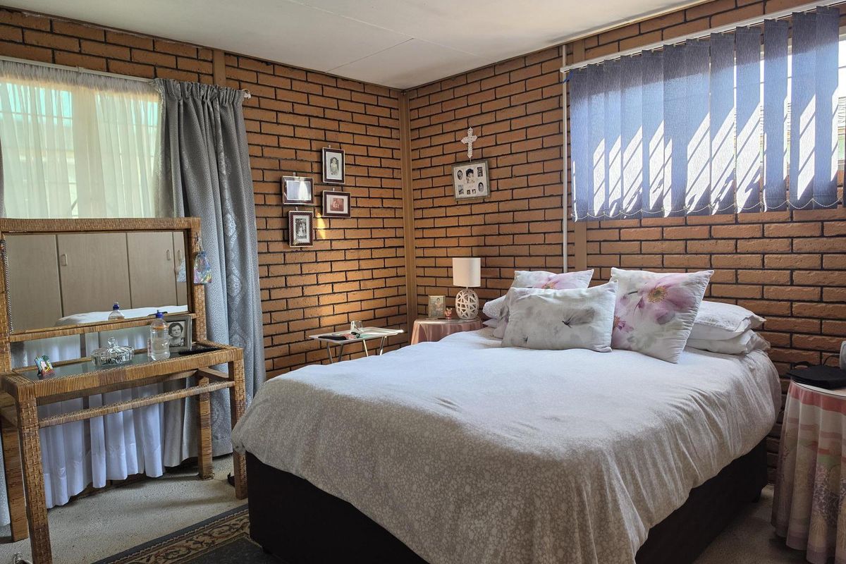 A bedroom featuring exposed brick walls, built-in storage cupboards, and natural light through vertical blinds.