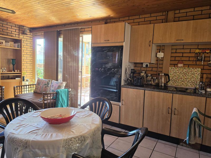Open plan kitchen and living area featuring exposed brick walls, timber ceiling, built-in oven, and direct access to the outdoor patio through sliding glass doors.