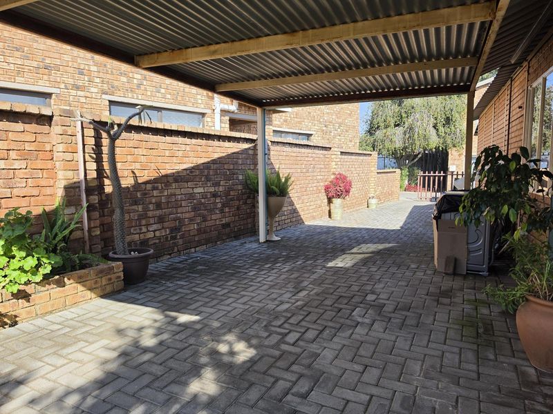 A covered carport area featuring a corrugated metal roof, brick boundary walls, and paved flooring, providing secure off-street parking.
