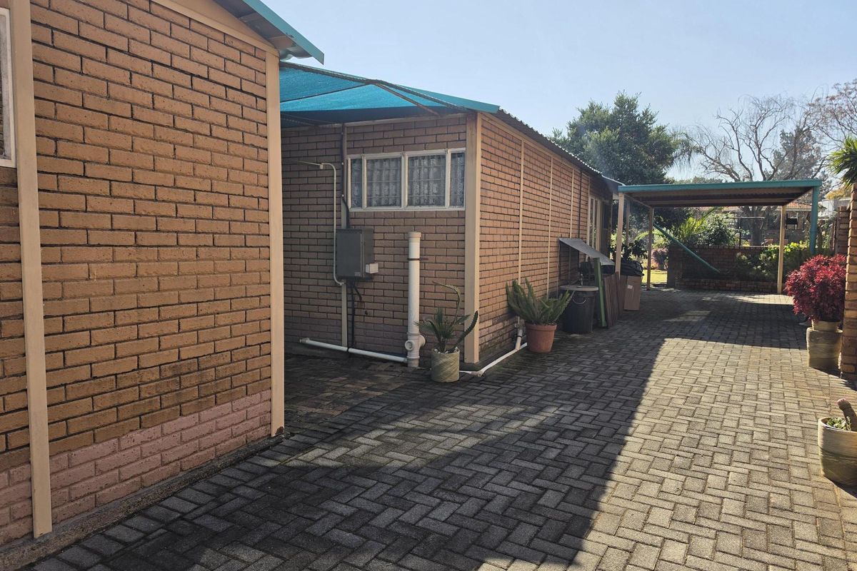 Rear exterior view of the property featuring face brick walls, a paved driveway, and a covered outdoor area with shade cloth.