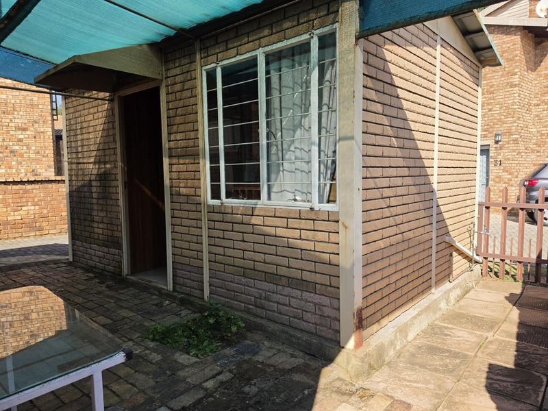 A view of the rear exterior featuring brick wall construction, security window bars, and a paved patio area with a shade cloth awning.