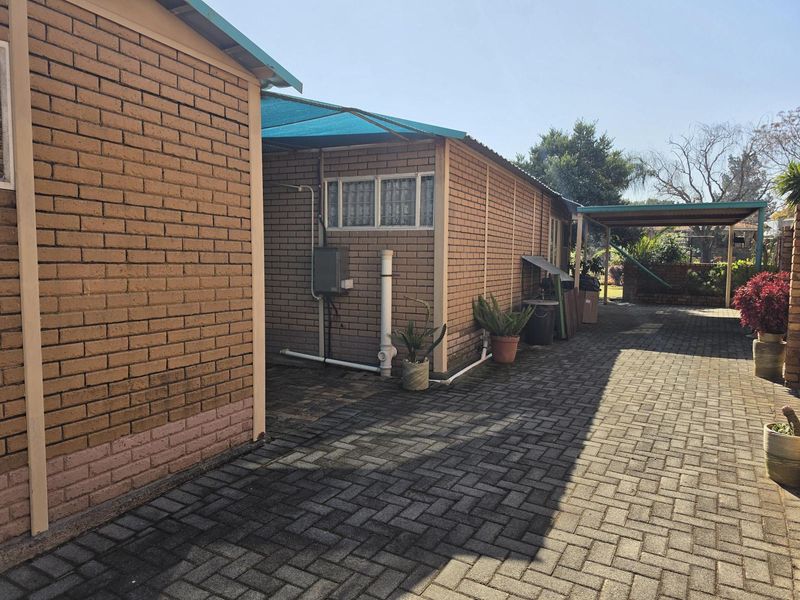 Rear exterior view of the property featuring brick walls, paved driveway, and a shade cloth covered area.